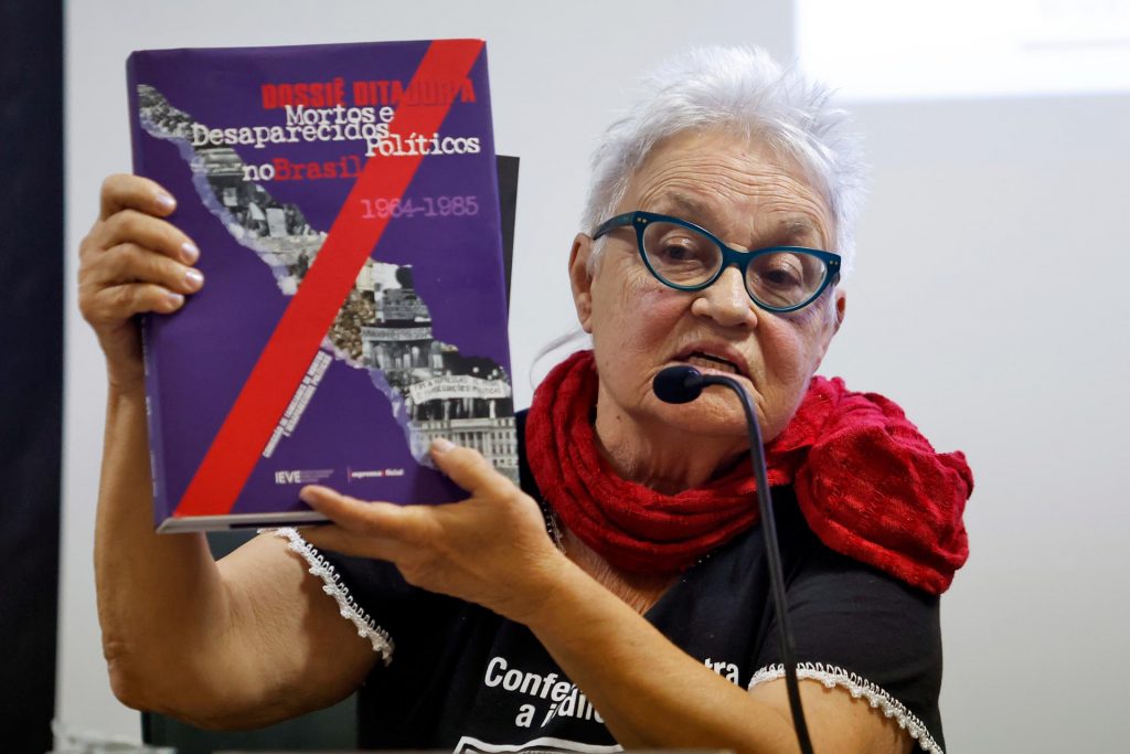 Maria Amélia Teles, a Amelinha, é uma referência na luta por justiça de transição com perspectiva de gênero no Brasil. Militante presa e torturada durante a ditadura militar, foi uma das primeiras mulheres a denunciar publicamente a violência sexual praticada por agentes do Estado. Sua atuação tem sido fundamental para o reconhecimento dessas violências como crimes contra a humanidade. Na imagem, Amelinha representa a Comissão de Familiares de Mortos e Desaparecidos Políticos durante coletiva de imprensa na UNIFESP, em que foram anunciadas as identificações de Denis Casemiro e Grenaldo de Jesus Silva — desaparecidos políticos da ditadura. Fonte: Agência Brasil. Autoria: Paulo Pinto.